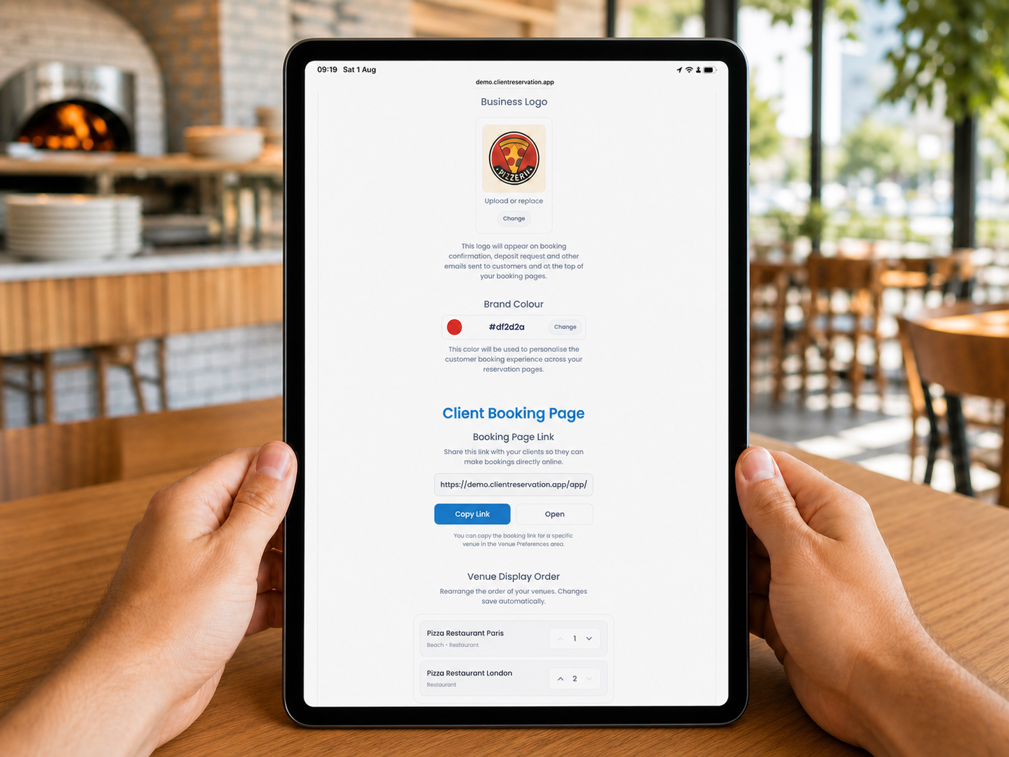 Client Reservation business branding settings displayed on a portrait iPad resting on a table in a modern pizza restaurant